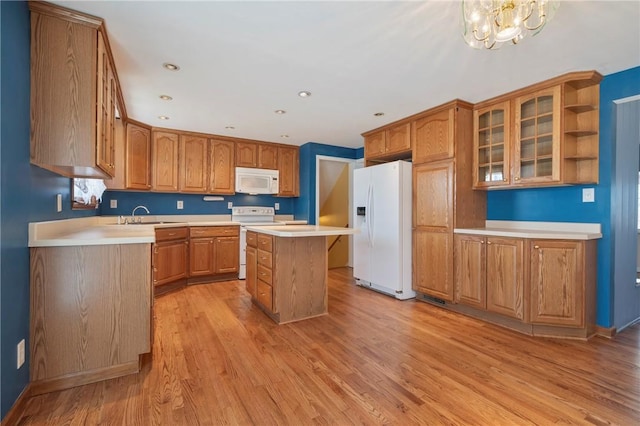 kitchen featuring a sink, a kitchen island, white appliances, light countertops, and glass insert cabinets