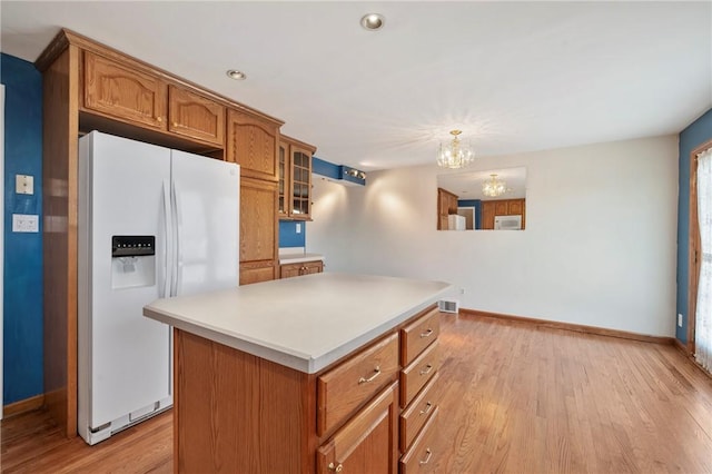 kitchen with brown cabinetry, a chandelier, light wood-style flooring, and white appliances