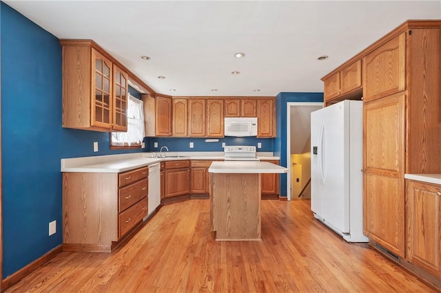 kitchen with white appliances, a kitchen island, a sink, light countertops, and glass insert cabinets