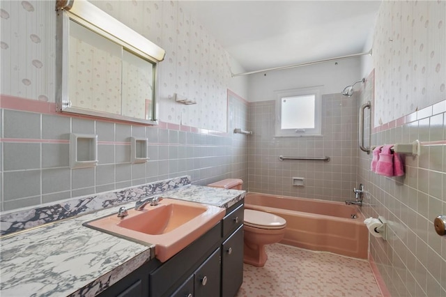 bathroom featuring wallpapered walls, a wainscoted wall, toilet, bathing tub / shower combination, and tile walls