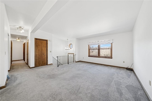 carpeted spare room with baseboards and a chandelier