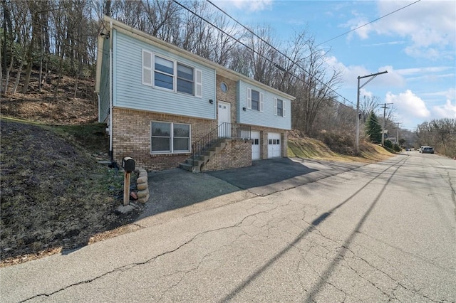 raised ranch featuring aphalt driveway, brick siding, and an attached garage