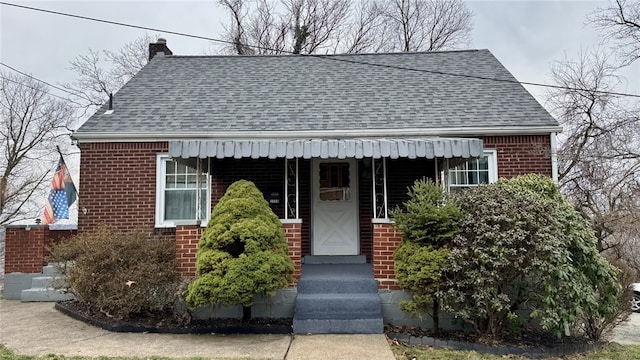 view of front of home featuring brick siding, a chimney, and a shingled roof