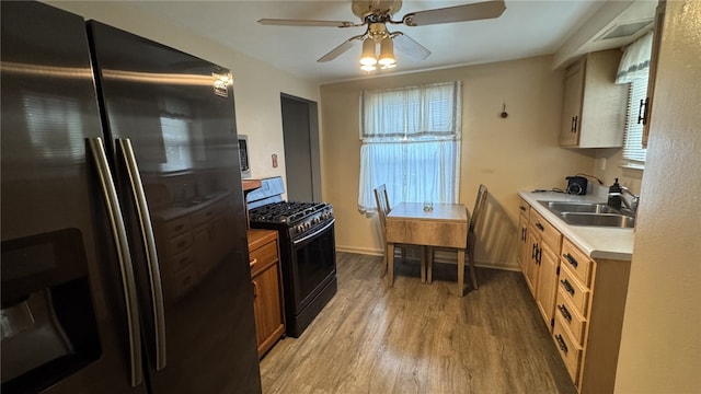 kitchen featuring black range with gas stovetop, light wood-type flooring, light countertops, stainless steel fridge, and a ceiling fan