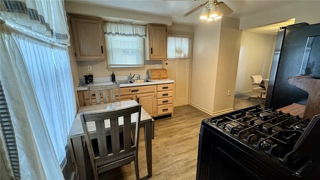 kitchen featuring light countertops, light wood-style floors, gas stove, a ceiling fan, and a sink