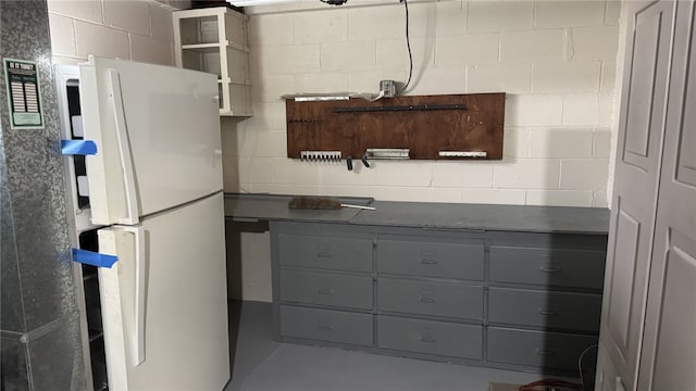 kitchen featuring gray cabinets, open shelves, dark countertops, freestanding refrigerator, and concrete block wall