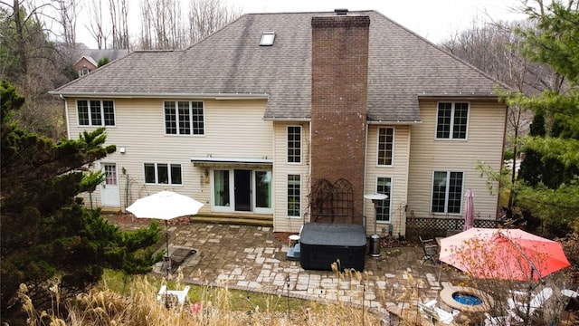 rear view of house with a patio, roof with shingles, and a chimney