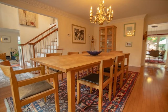 dining space with hardwood / wood-style floors, stairs, an inviting chandelier, and ornamental molding