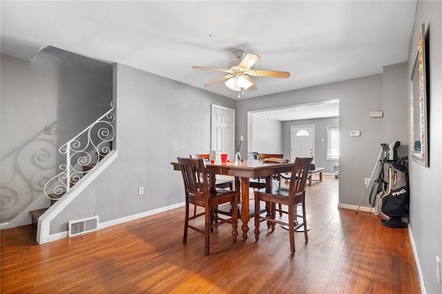 dining space featuring hardwood / wood-style floors, baseboards, visible vents, ceiling fan, and stairs