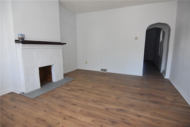 unfurnished living room with arched walkways, visible vents, a brick fireplace, and wood finished floors