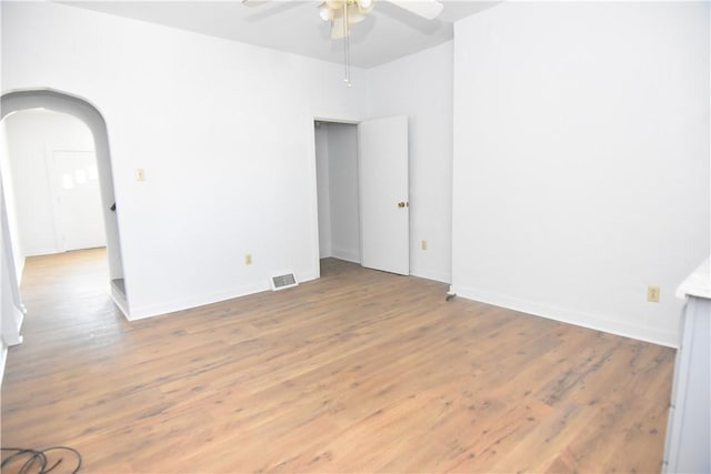 unfurnished room with visible vents, baseboards, ceiling fan, light wood-style floors, and arched walkways