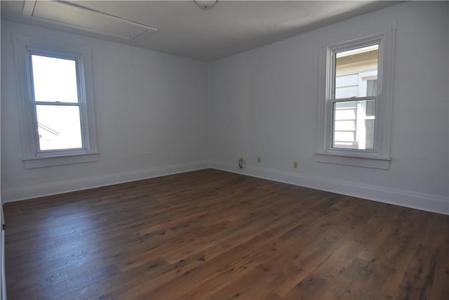 unfurnished room with attic access, dark wood-type flooring, and baseboards