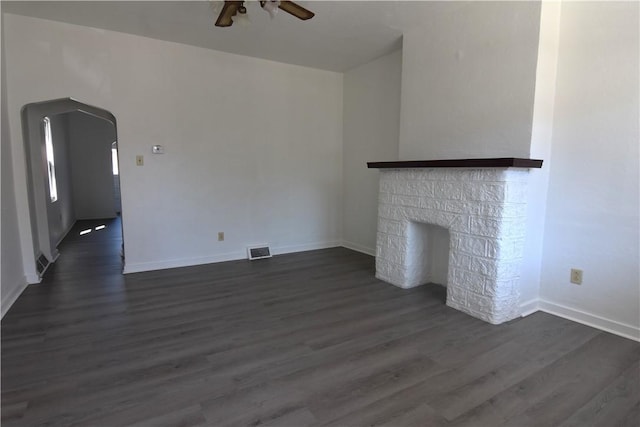 unfurnished living room with dark wood-style floors, a ceiling fan, visible vents, a fireplace, and arched walkways