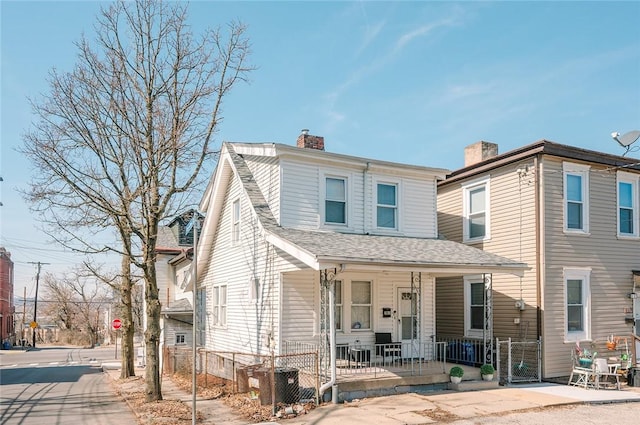 multi unit property with a fenced front yard, roof with shingles, a porch, and a chimney