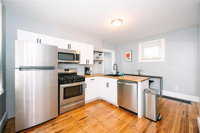 kitchen featuring visible vents, appliances with stainless steel finishes, light wood-style floors, white cabinets, and a sink