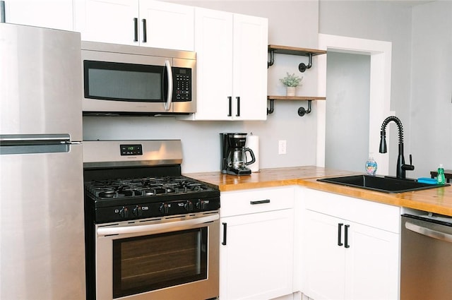 kitchen featuring a sink, butcher block countertops, appliances with stainless steel finishes, white cabinets, and open shelves