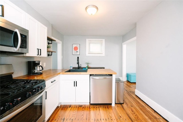 kitchen with a sink, stainless steel appliances, wooden counters, and a peninsula