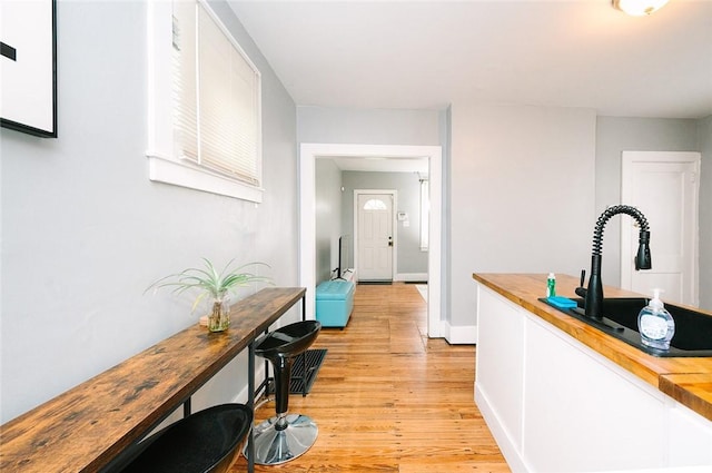 hall featuring light wood-style floors, baseboards, and a sink