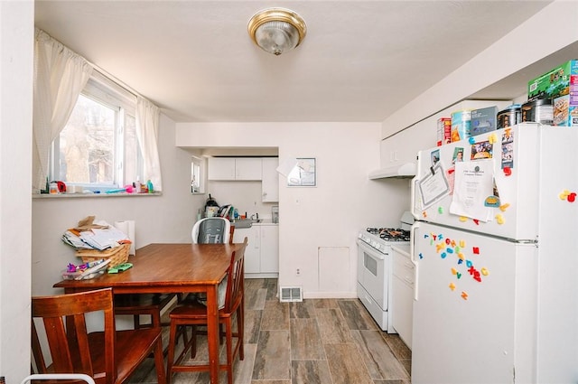 kitchen with white appliances, visible vents, wood tiled floor, white cabinets, and under cabinet range hood