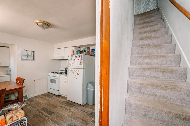 interior space featuring visible vents, under cabinet range hood, white appliances, white cabinets, and baseboards