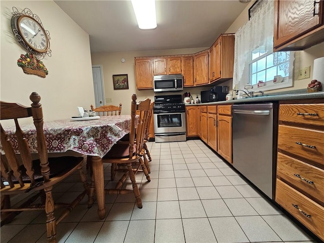 kitchen featuring light tile patterned flooring, stainless steel appliances, and brown cabinetry