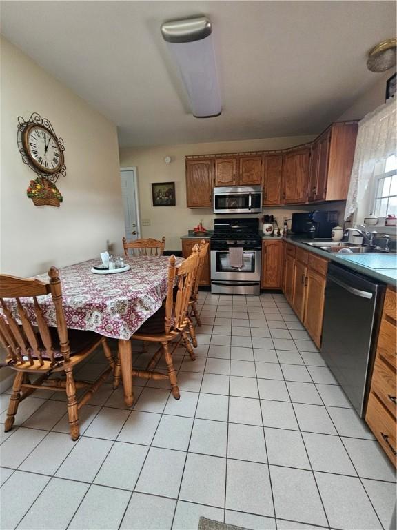 kitchen featuring light tile patterned floors, brown cabinetry, appliances with stainless steel finishes, and a sink