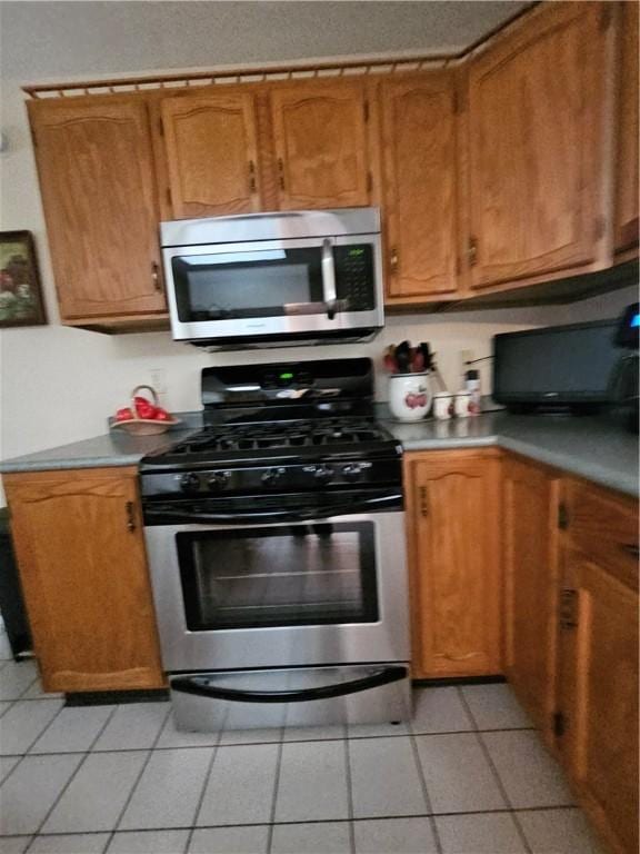 kitchen featuring light countertops, light tile patterned floors, brown cabinetry, and stainless steel appliances