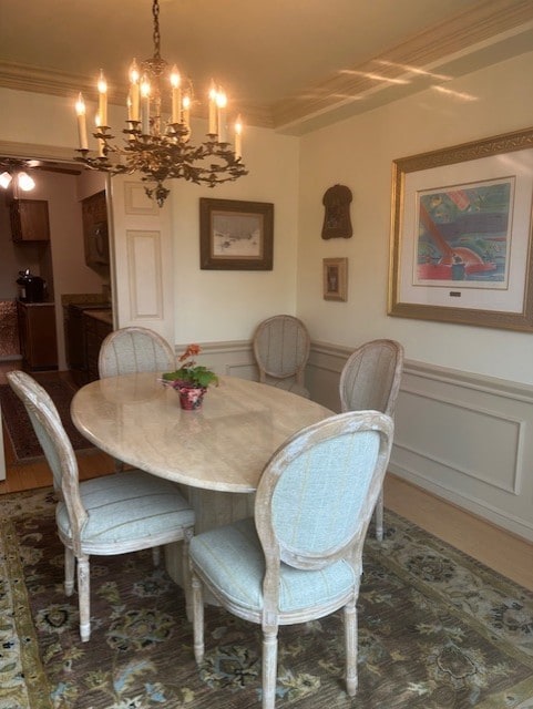 dining area featuring a decorative wall, wainscoting, an inviting chandelier, and ornamental molding