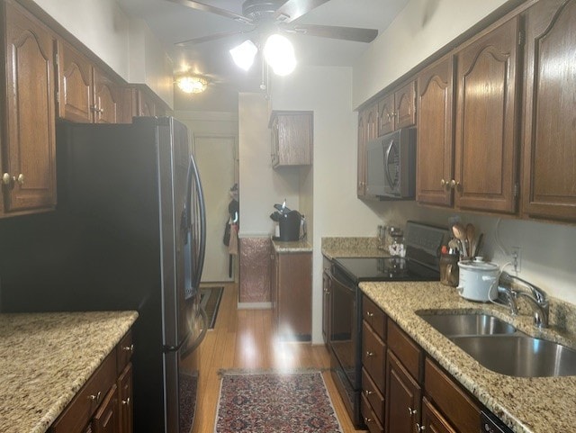 kitchen featuring light stone counters, a ceiling fan, a sink, appliances with stainless steel finishes, and light wood-type flooring