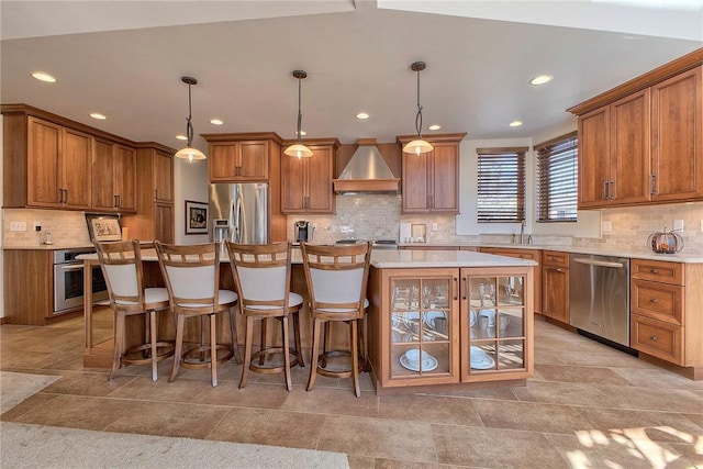 kitchen featuring brown cabinets, a sink, tasteful backsplash, stainless steel appliances, and wall chimney range hood