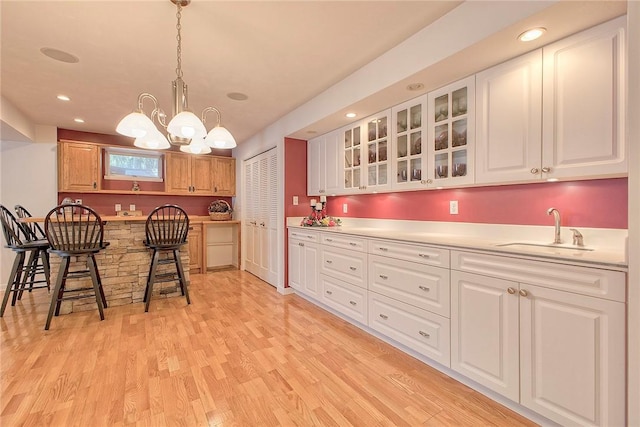 kitchen with a sink, a kitchen breakfast bar, light wood finished floors, glass insert cabinets, and a chandelier