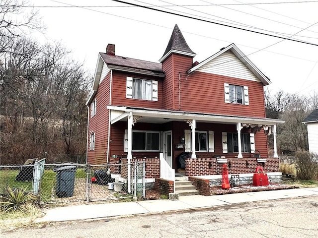 view of front of house featuring a gate, a porch, a chimney, and fence