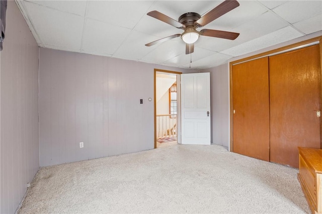 unfurnished bedroom with a closet, a drop ceiling, ceiling fan, and carpet