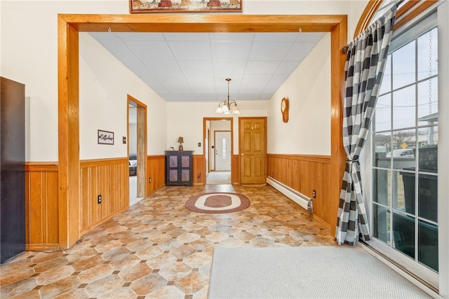 foyer entrance featuring a wainscoted wall, a baseboard radiator, an inviting chandelier, wood walls, and stone finish flooring