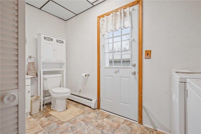 bathroom with a baseboard radiator, stone finish floor, toilet, washing machine and dryer, and baseboard heating