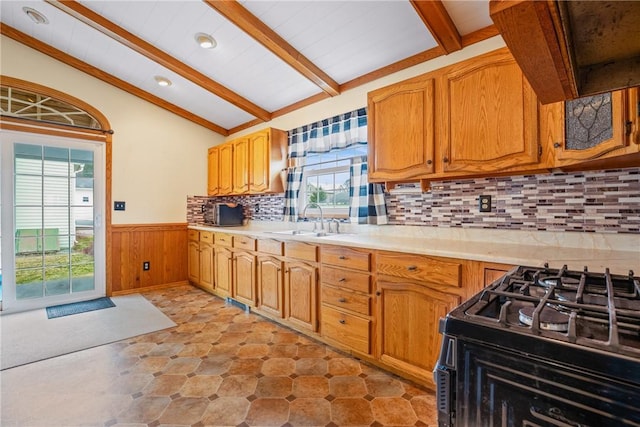 kitchen featuring a sink, lofted ceiling with beams, wainscoting, light countertops, and black range with gas cooktop