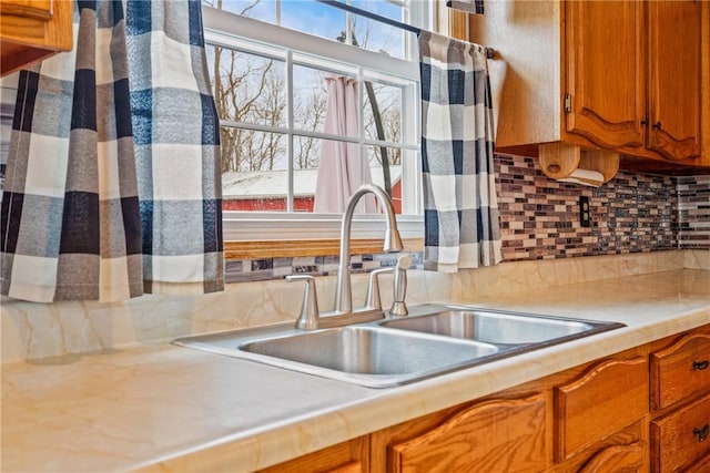 kitchen featuring light countertops, brown cabinetry, backsplash, and a sink