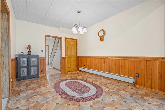 interior space featuring an inviting chandelier, wood walls, wainscoting, a baseboard radiator, and stairs