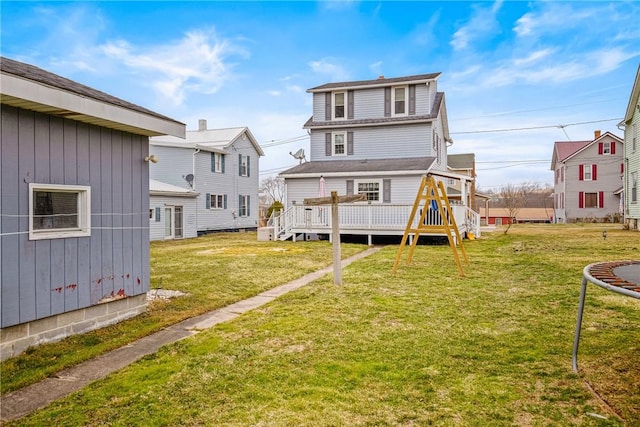 back of house with a deck, a trampoline, and a lawn