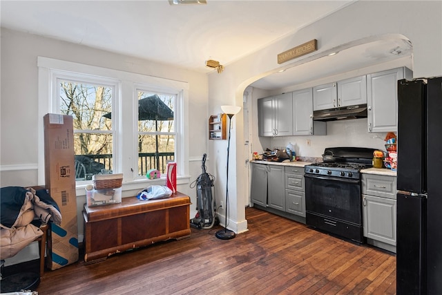 kitchen featuring gray cabinetry, under cabinet range hood, light countertops, black appliances, and dark wood-style flooring