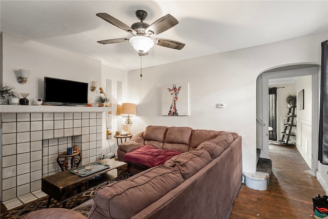 living area featuring arched walkways, a fireplace, ceiling fan, and wood finished floors