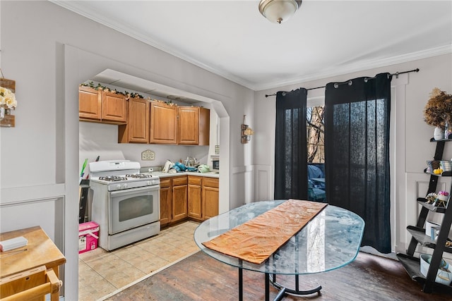 kitchen featuring light countertops, white range with gas stovetop, brown cabinetry, and ornamental molding