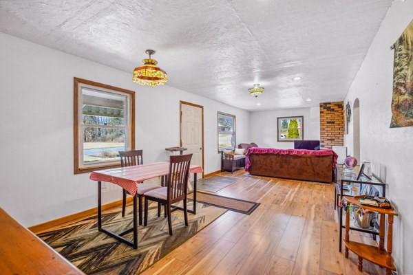 dining room with arched walkways, a textured ceiling, light wood-type flooring, and baseboards