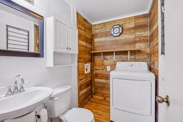 half bathroom with washer / dryer, wooden walls, toilet, and a sink