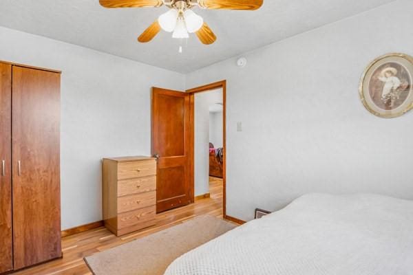 bedroom featuring light wood-type flooring, baseboards, a closet, and a ceiling fan