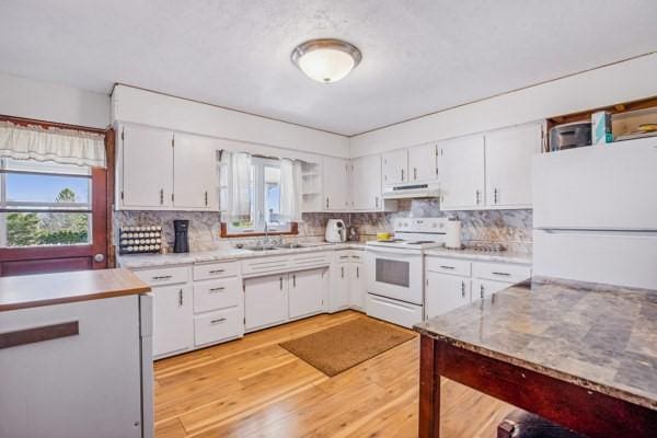 kitchen with white appliances, a wealth of natural light, light wood finished floors, and under cabinet range hood