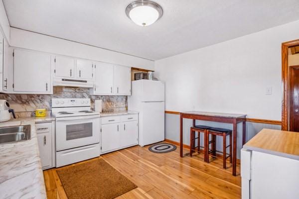 kitchen with light wood-style flooring, under cabinet range hood, white cabinetry, white appliances, and light countertops