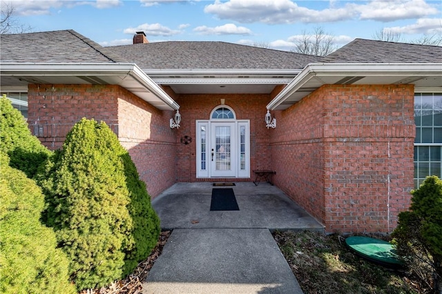 property entrance featuring brick siding, a chimney, and roof with shingles