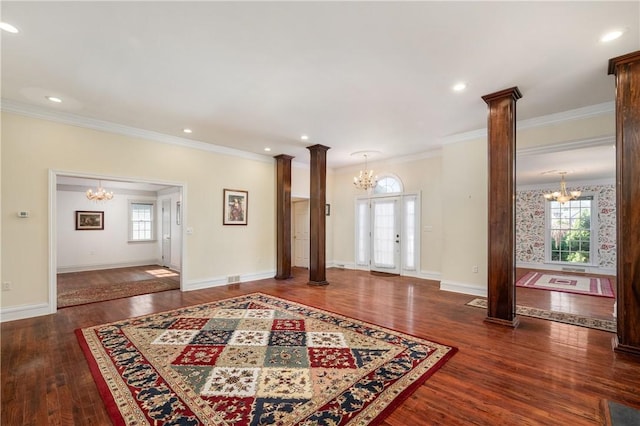 foyer entrance featuring ornamental molding, wood finished floors, an inviting chandelier, and decorative columns