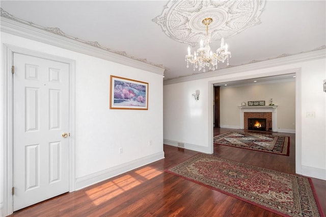 interior space with wood finished floors, baseboards, a fireplace, crown molding, and a chandelier